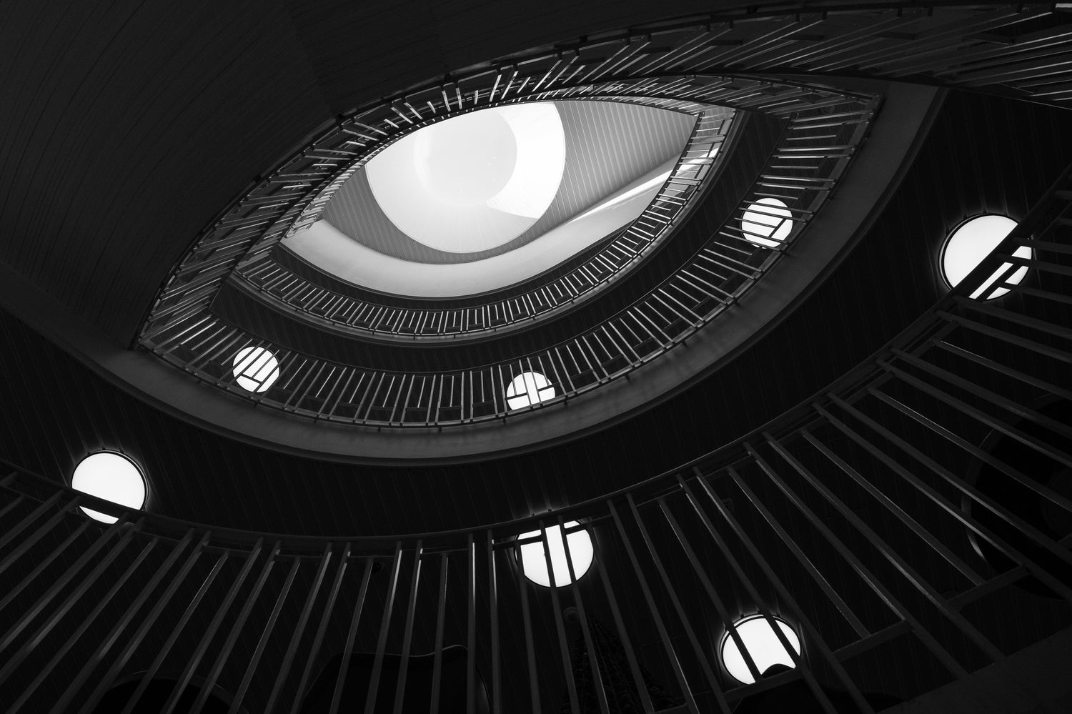 A staircase in Helsinki, cast in black-and-white style, reminiscent of an eye. The eye is connected to George Orwell because of the fear of secret police that pervades his work, whose watchful eye we all must fear. Photo by Petri Heiskanen on Unsplash.