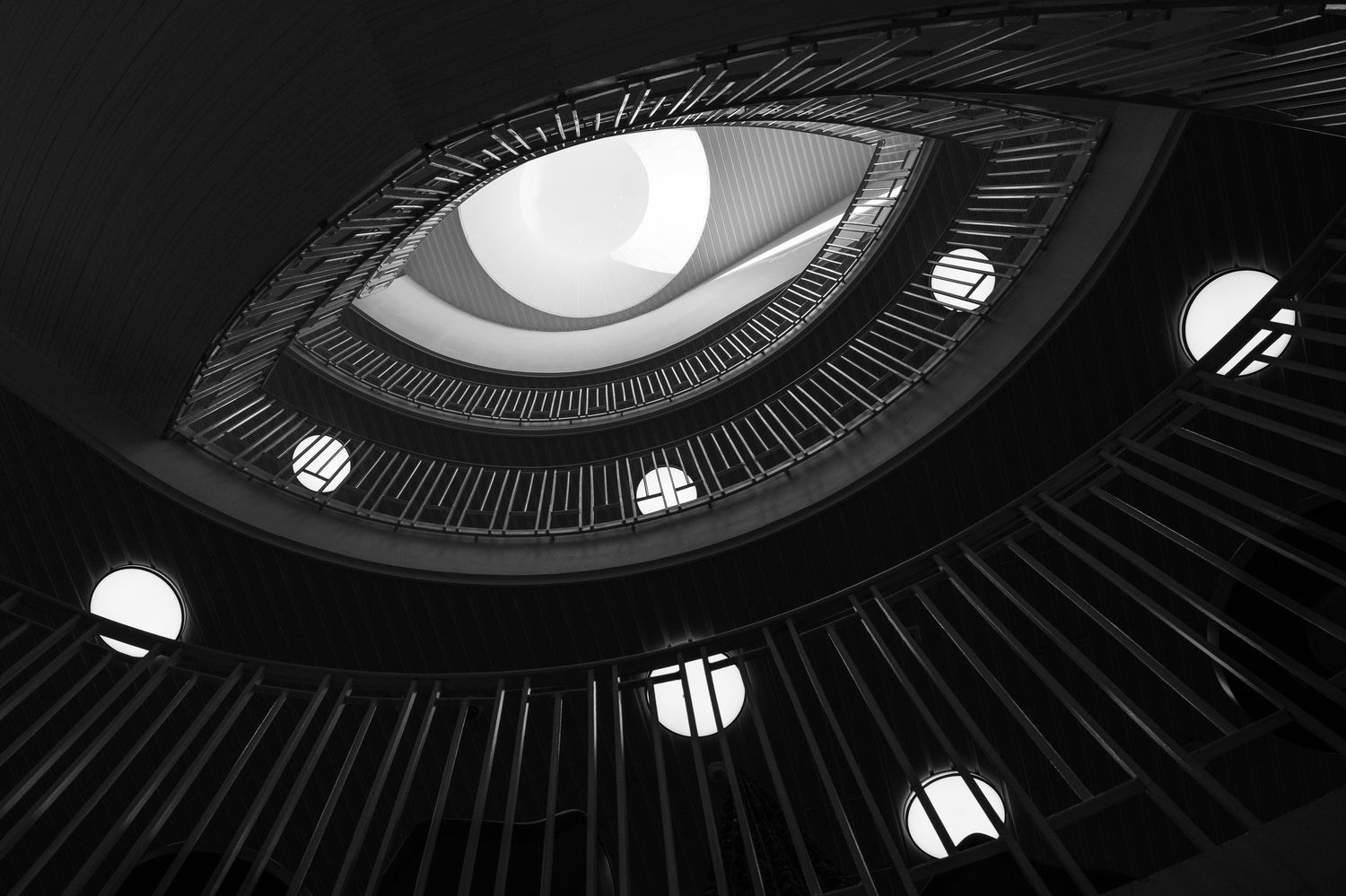 A staircase in Helsinki, cast in black-and-white style, reminiscent of an eye. The eye is connected to George Orwell because of the fear of secret police that pervades his work, whose watchful eye we all must fear. Photo by Petri Heiskanen on Unsplash.